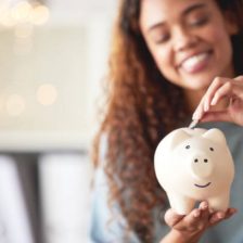 One happy young mixed race woman holding a piggybank and depositing a coin as savings. Hispanic woman budgeting her finances and investing money into her future. Saving funds for financial freedom